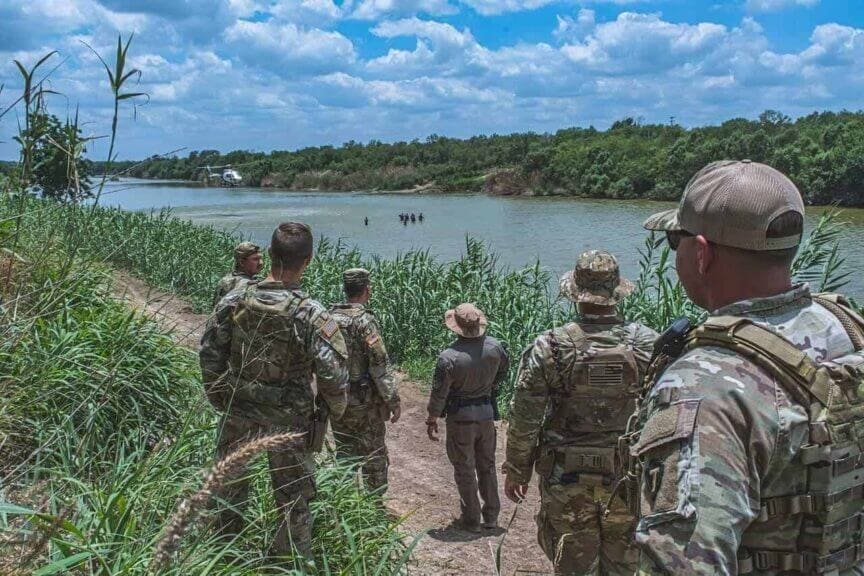 img 7237 Members of the texas national guard watch a border patrol helicopter hover above a group of civilians wading in the rio grande along the texas-mexico border during operation lone star.