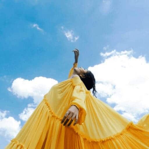 img 7292 Model wearing a yellow dress points up at a bright blue sky with white fluffy clouds